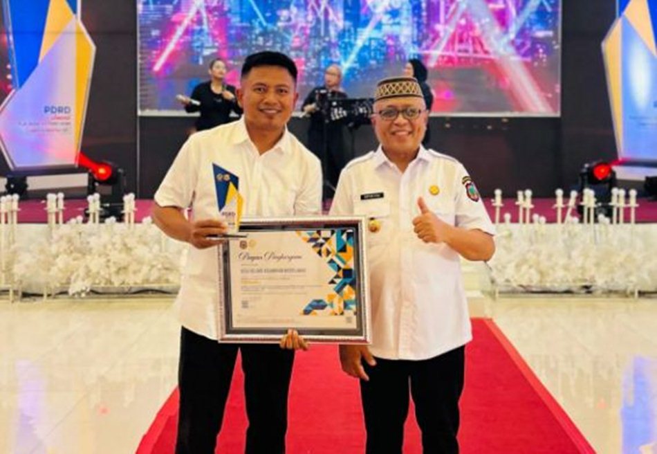 Kepala Desa Helumo, Habri Mahmud, S.Pd, menerima langsung penghargaan dari Bupati Sofyan Puhi.(F:Kmfo)