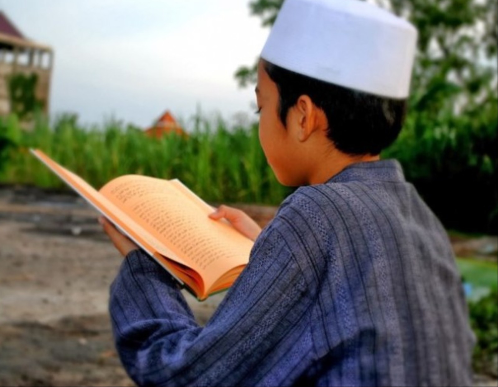 Seorang santri tampak sedang mengaji atau menghafal kitab suci alquran di balik dinding ponpes yang sederhana.