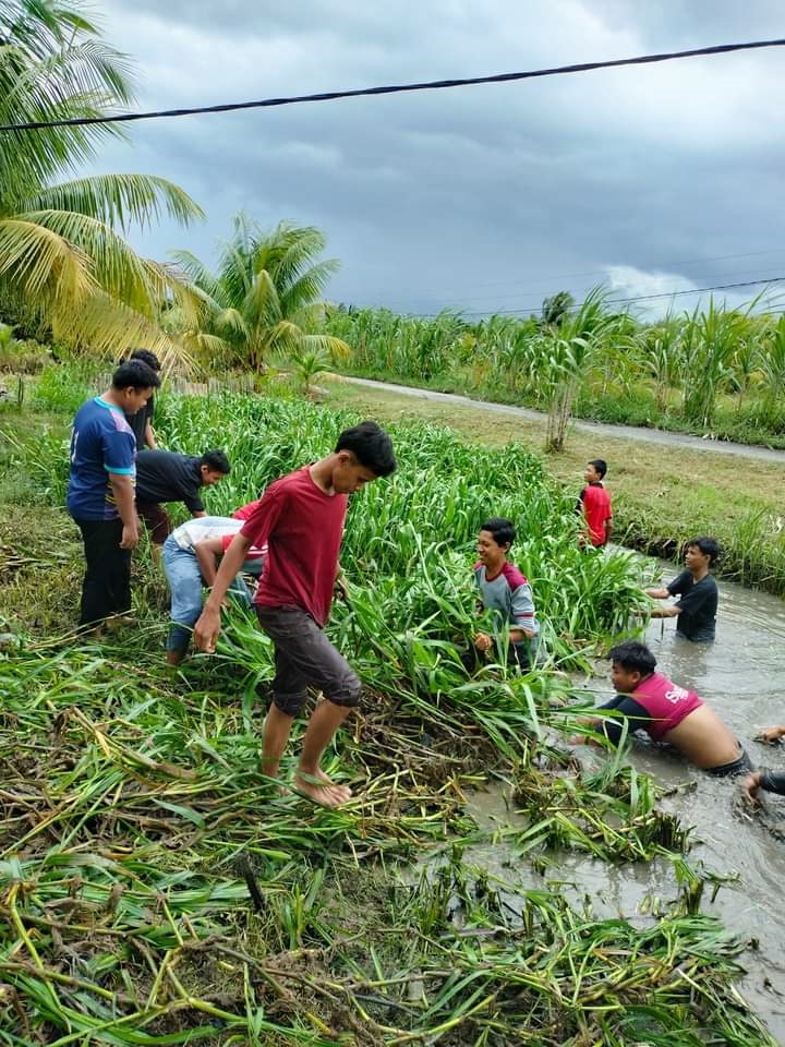 Foto: Warga bersama pelajar saat turun ke parit membersihkan tanaman liar yang mengganggu pembuangan air.