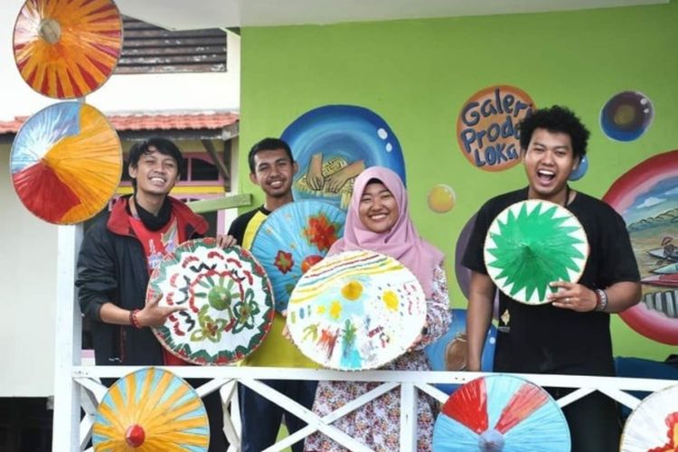 Anak-anak muda sedang berada di Rumah Ide sambil berpose bersama caping yang dihias dan berwarna-warni.