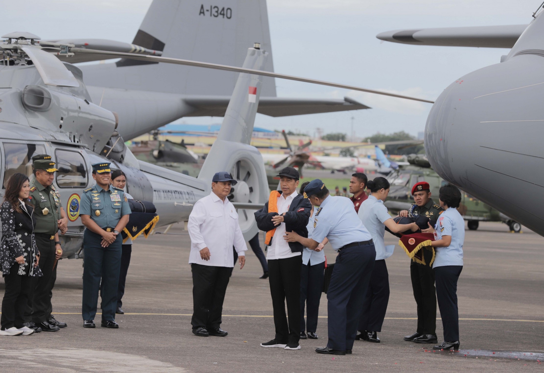 Presiden Jokowi dipakaikan jaket oleh Menhan Prabowo dan KSAU Marsekal TNI Fadjar Prasetyo (kanan) saat serah terima alutsista pesawat dari pemerintah untuk TNI di Lanud Halim, Rabu (24/1).