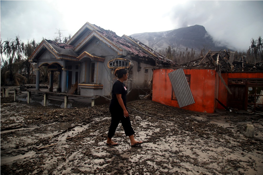 Warga berjalan di depan rumah yang rusak parah terdampak erupsi Gunung Ruang di Desa Laingpatehi Pulau Ruang, Kabupaten Kepulauan Sitaro, Sulawesi Utara, Jumat (3/5/2024).