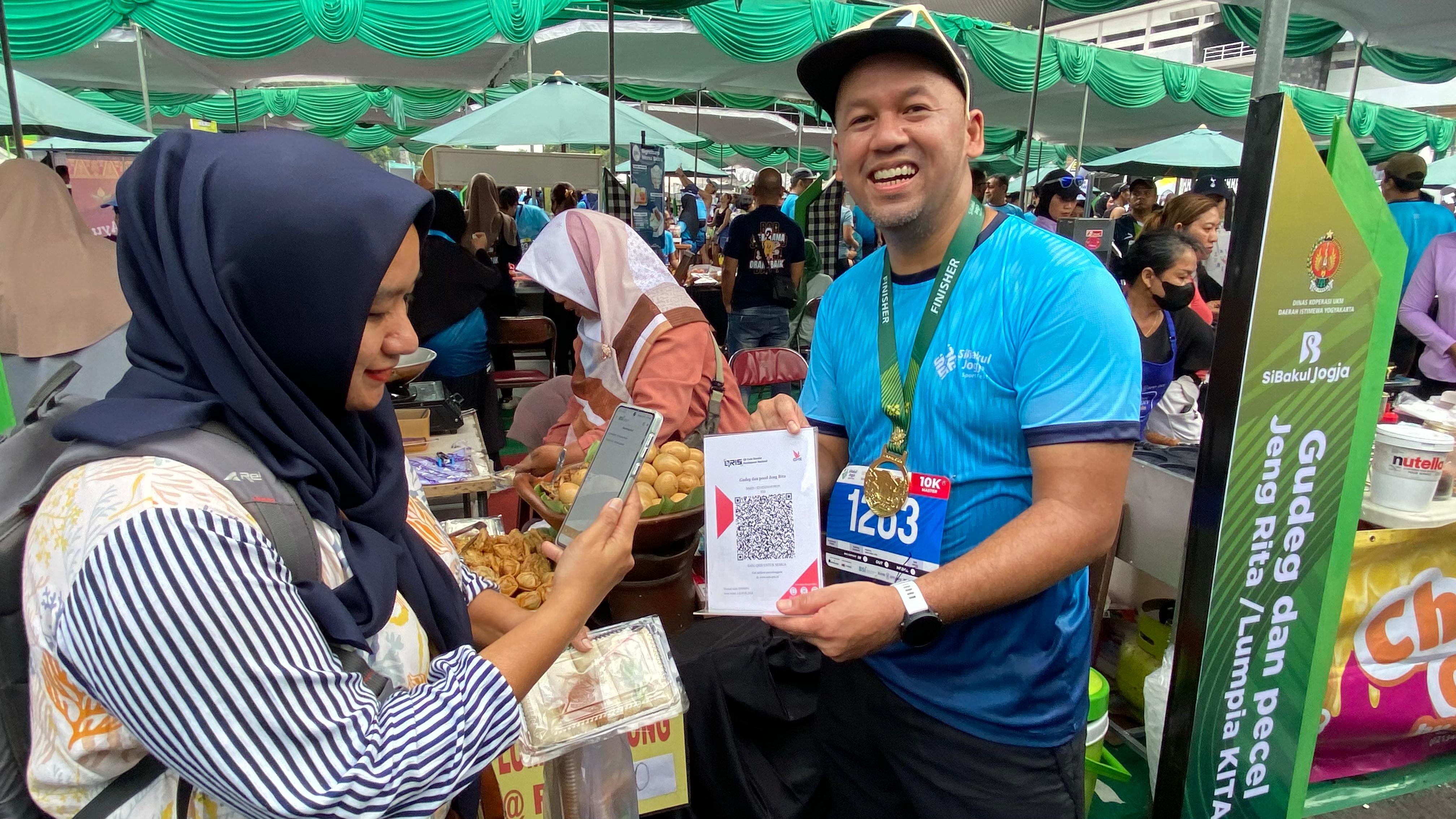 Direktur Finance & Strategy BSI Ade Cahyo Nugroho (kanan) saat melayani translaksi pembayaran QRIS pengunjung pada gelaran acara Sibakul Jogja Sport Fest 2024 di salah satu tenant UMKM.