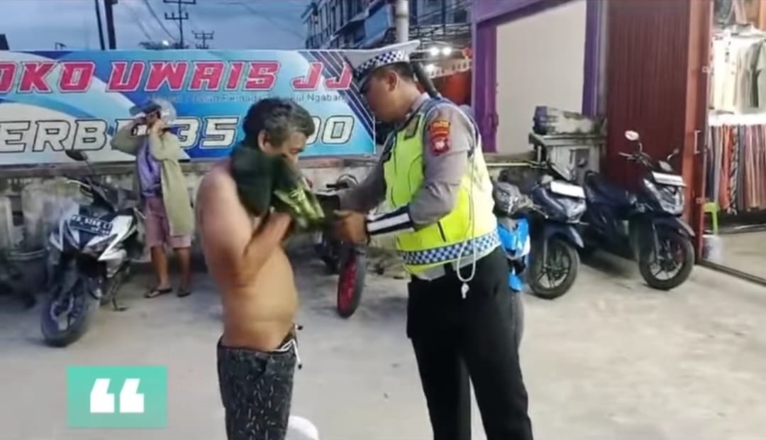 BANTUAN: Aipda Harry, anggota Polantas Polres Landak saat membantu seorang ODGJ mengenakan baju.
