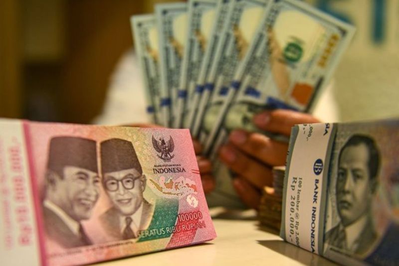 Petugas perbankan menunjukan uang pecahan dolar AS dan rupiah. 