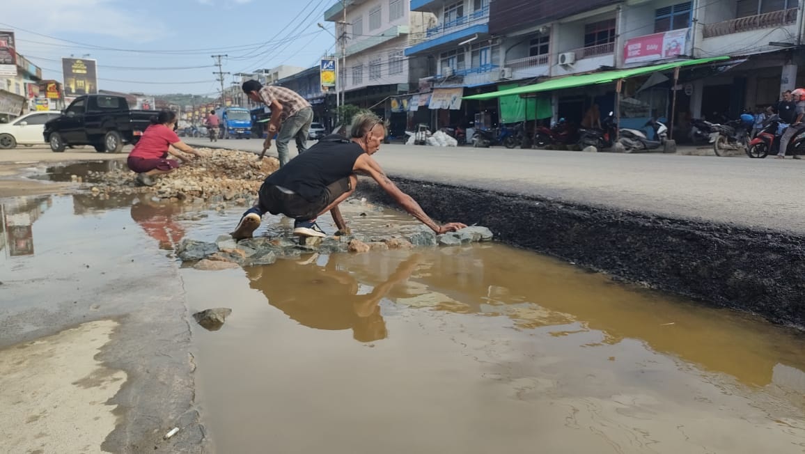 TIMBUN: Pengusaha ruko di jalan jurusan Sungai Pinyuh-Mempawah terpaksa membeli batu untuk menimbun bahu jalan yang tinggi.