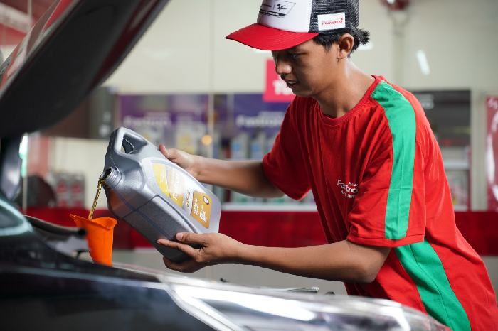 Seorang mekanik sedang melakukan penggantian oli pada mobil.