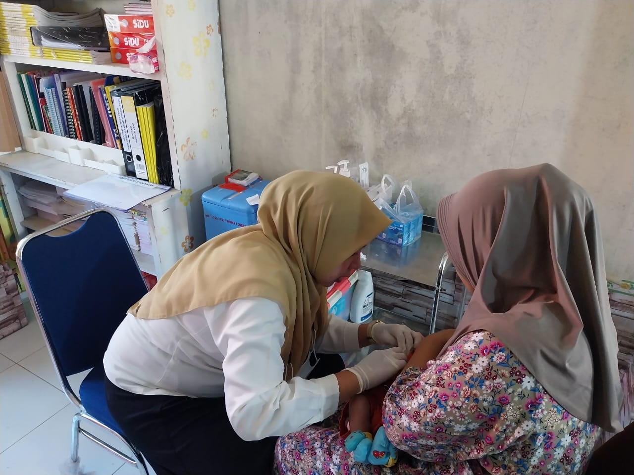IMUNISASI: Salah satu petugas kesehatan di puskesmas di Singkawang sedang memberikan imunisasi kepada seorang balita yang tengah didekap ibunya.
