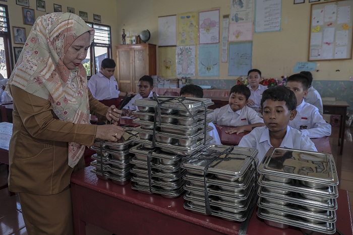 Seorang guru bersiap membagikan ompreng berisi makanan program Makan Bergizi Gratis (MBG) kepada siswa di SD Negeri 50 Kota Ternate, Maluku Utara, Selasa (30/9/2025). Presiden Prabowo Subianto mengatakan program MBG telah menjangkau hampir 30 juta penerim
