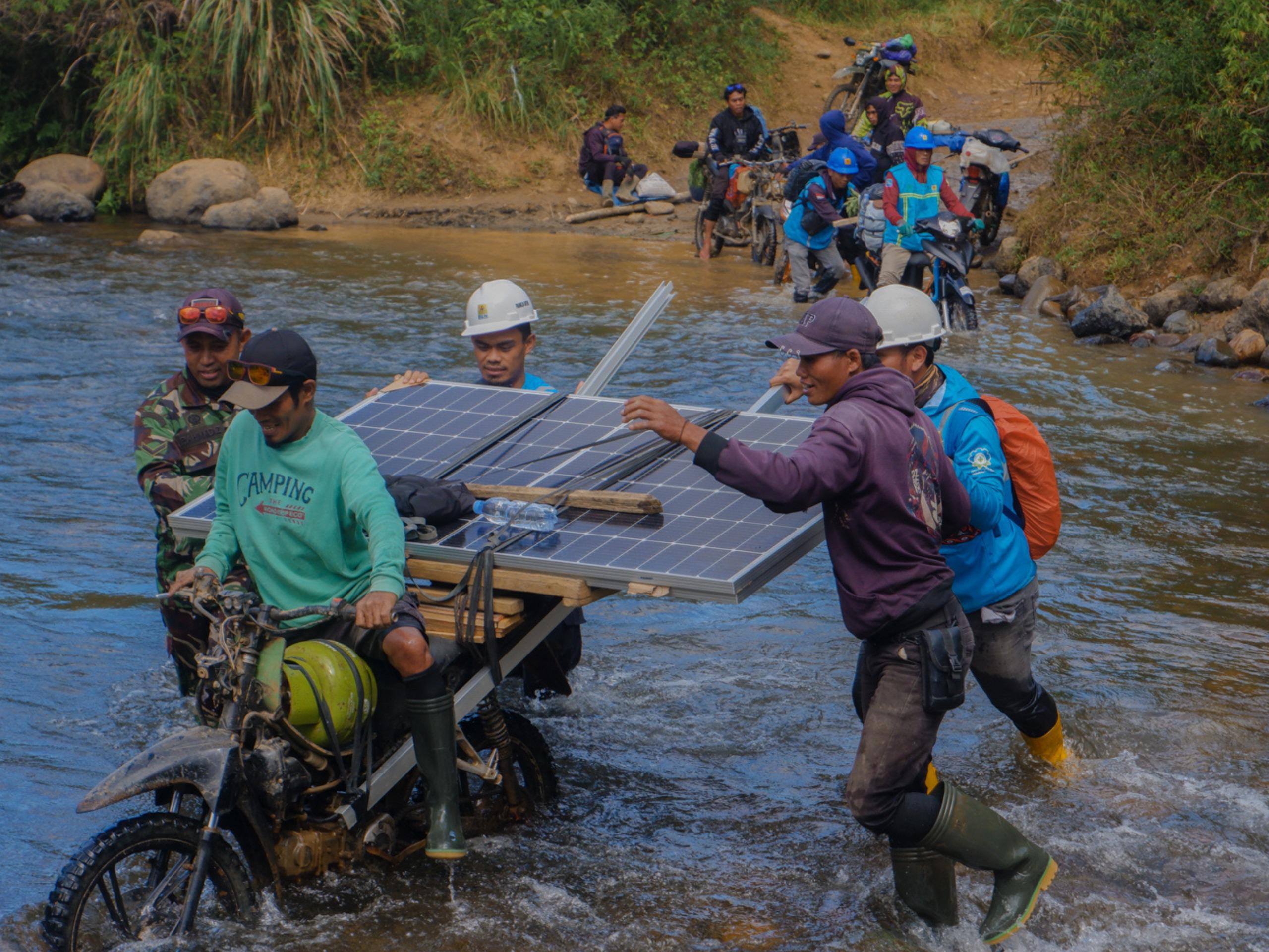 Petugas PLN bersama warga bahu-membahu membawa panel surya melintasi sungai. Upaya ini menjadi bagian dari perjalanan Program Listrik Desa (Lisdes) melalui SuperSUN dalam menghadirkan akses listrik ba
