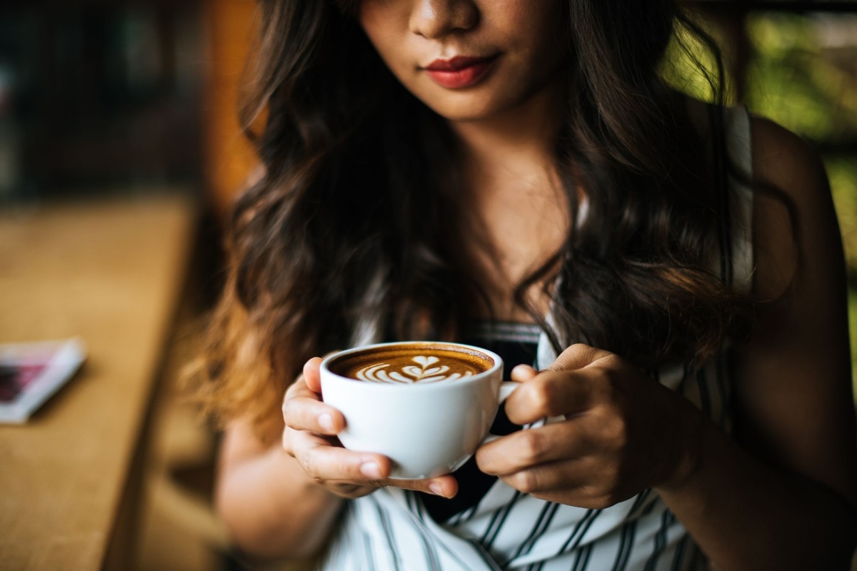 Ilustrasi seorang perempuan sedang menikmati secangkir kopi susu, minuman populer yang kini juga dikaitkan dengan potensi masalah kulit seperti breakout atau jerawat.