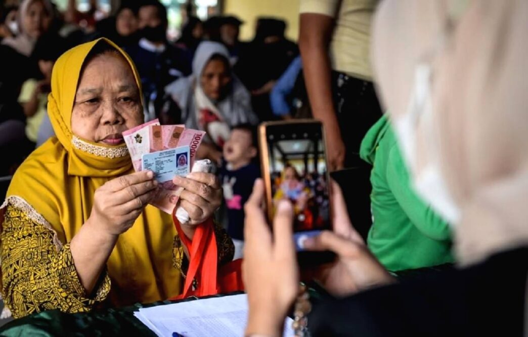 BANSOS: Petugas memotret warga memperlihatkan uang tunai saat penyaluran bantuan sosial beberapa waktu lalu.
