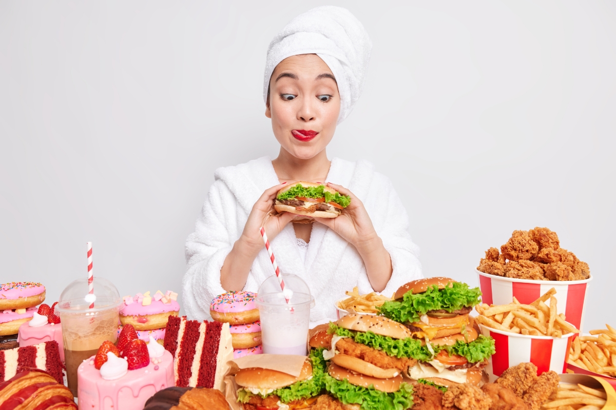Ilustrasi seorang wanita yang sedang menikmati makanan cepat saji seperti burger, ayam goreng, dan kue manis saat melakukan cheat day dalam program diet.