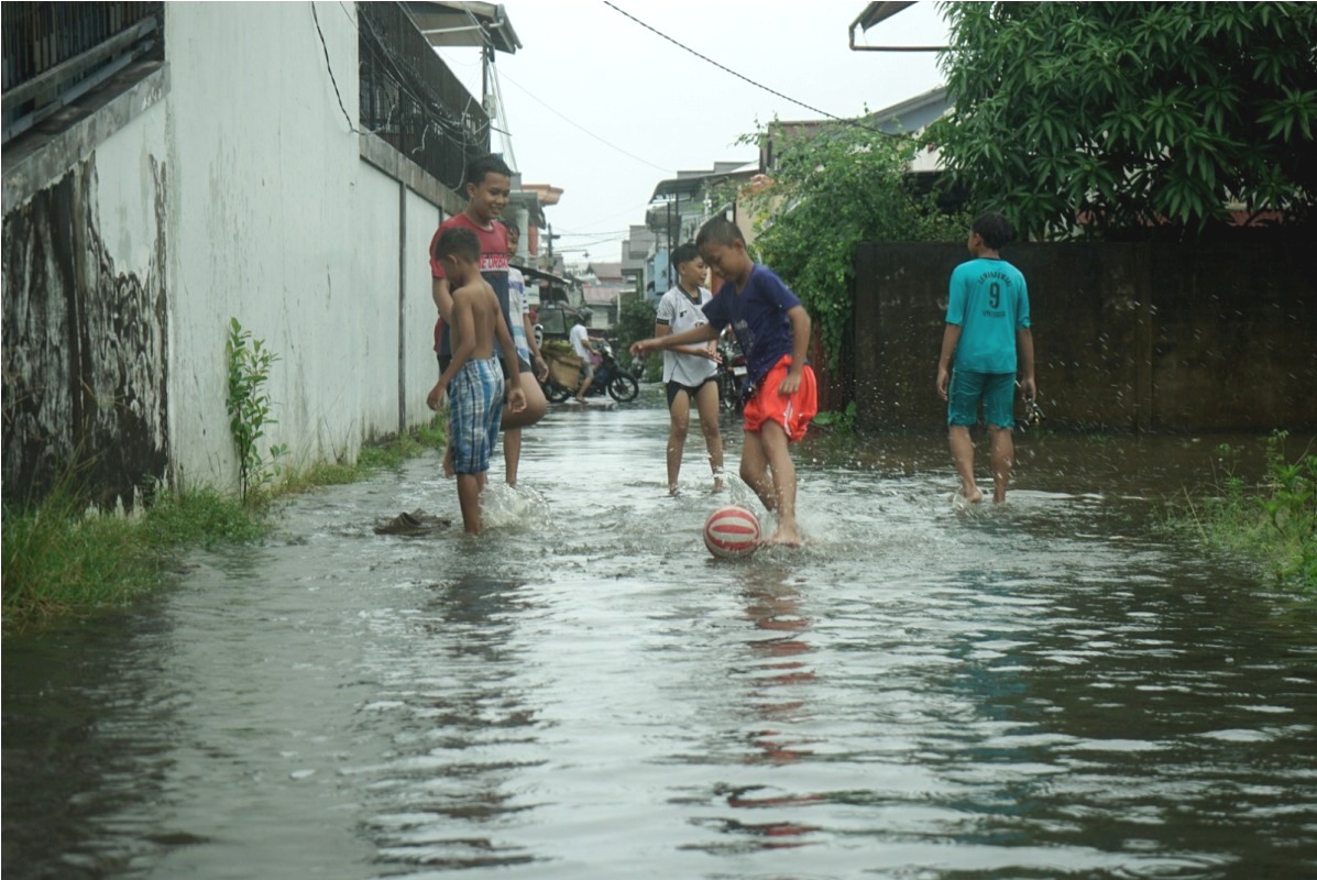 Anak-anak bermain bola digenangan air imbas pasang air laut dan hujan yang turun di Gang Ilham Jalan Veteran.