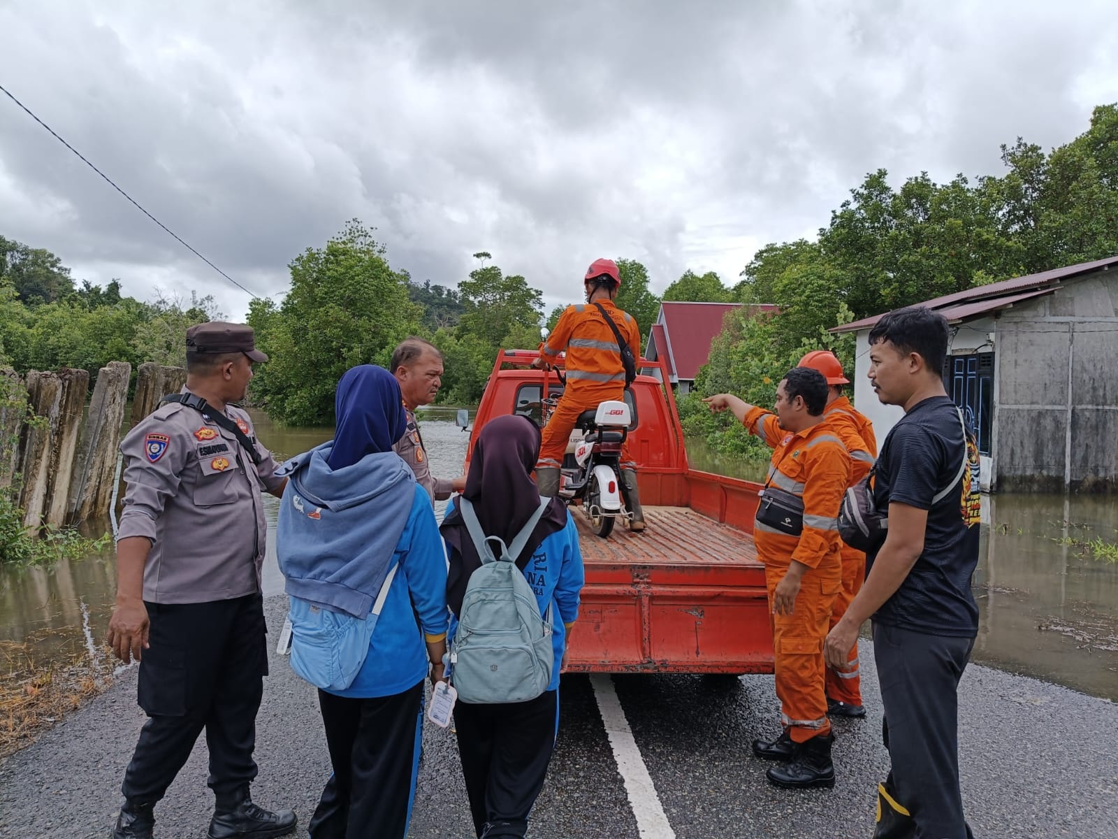BANTU : Personel kepolisian dan petugas tim SAR, membantu warga, termasuk menaikkan sepeda motor ke bak kendaraan untuk membantu mereka melintasi jalan yang terendam banjir.