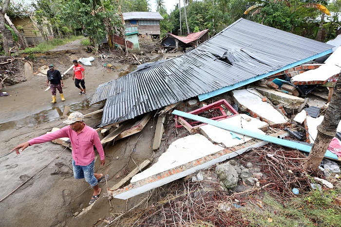 Warga melintas di dekat rumah yang hancur akibat bencana banjir bandang di Desa Alue Kuta, Kecamatan Jangka, Bireuen, Aceh, Minggu (14/12/2025). Data sementara posko tanggap darurat bencana hidrometeorologi Aceh menyebutkan sebanyak 1.232 unit rumah warga