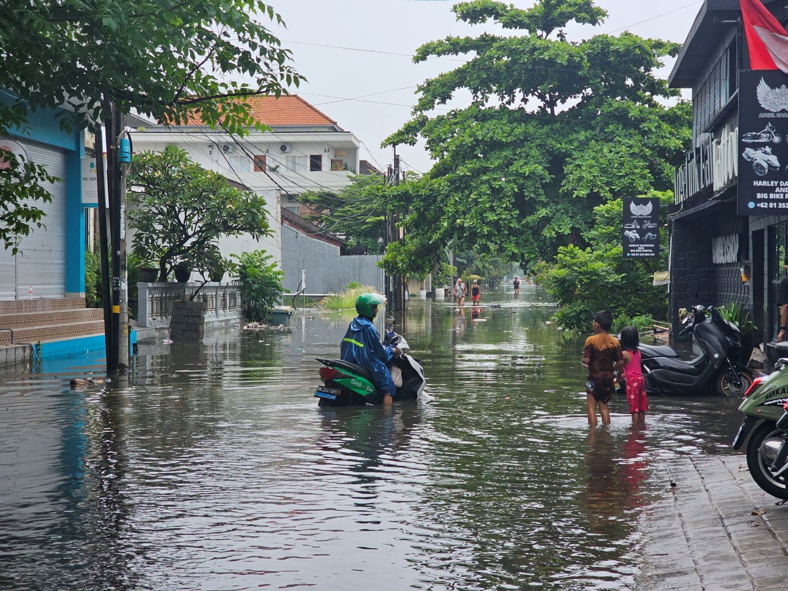 DAMPAK SIKLON: Warga Negara Asing melintas di genangan banjir di Legian dan anak-anak asyik bermain air kemarin (14/12/2025