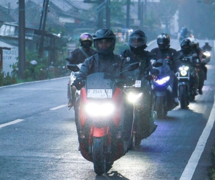 Pengendara sepeda motor tetap waspada dan menjaga keselamatan di tengah hujan deras.
