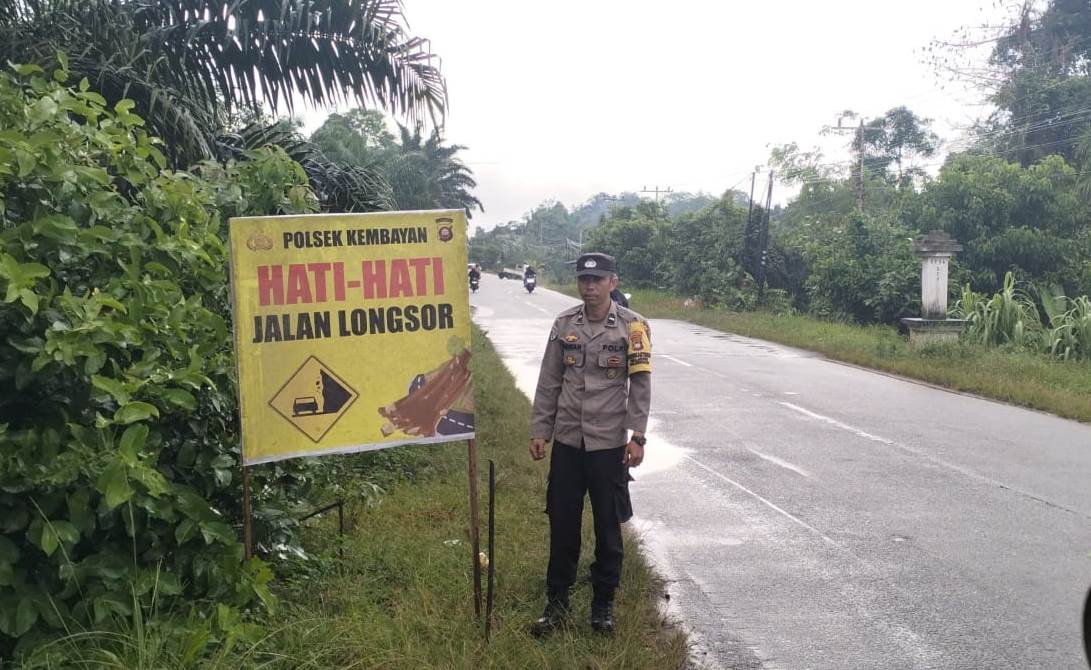 Personel Polsek Kembayan memasang papan peringatan jalan longsor di kawasan rawan guna mengingatkan pengguna jalan agar lebih waspada saat cuaca hujan.