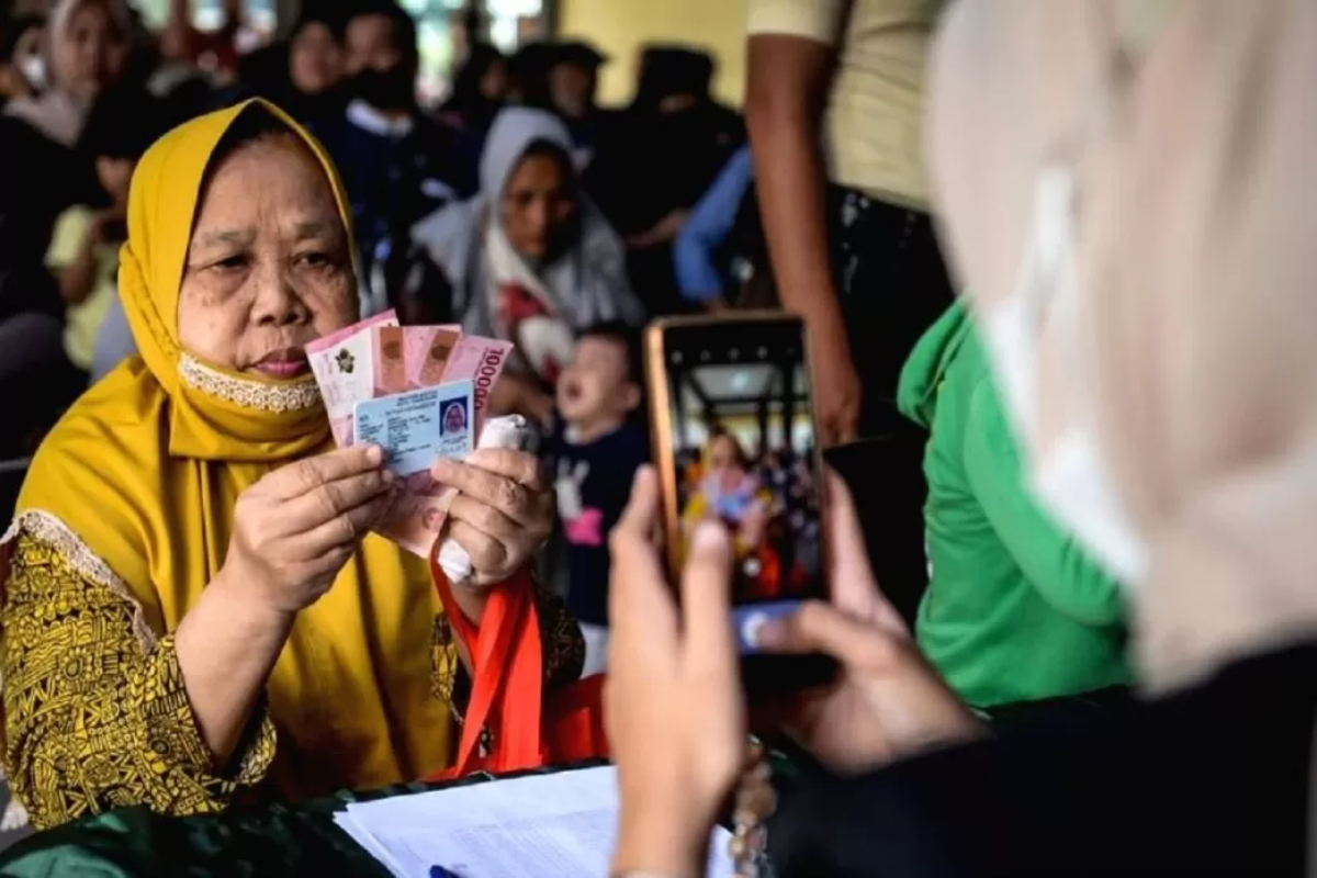 Petugas memotret warga memperlihatkan uang tunai saat penyaluran bantuan sosial beberapa waktu lalu. 