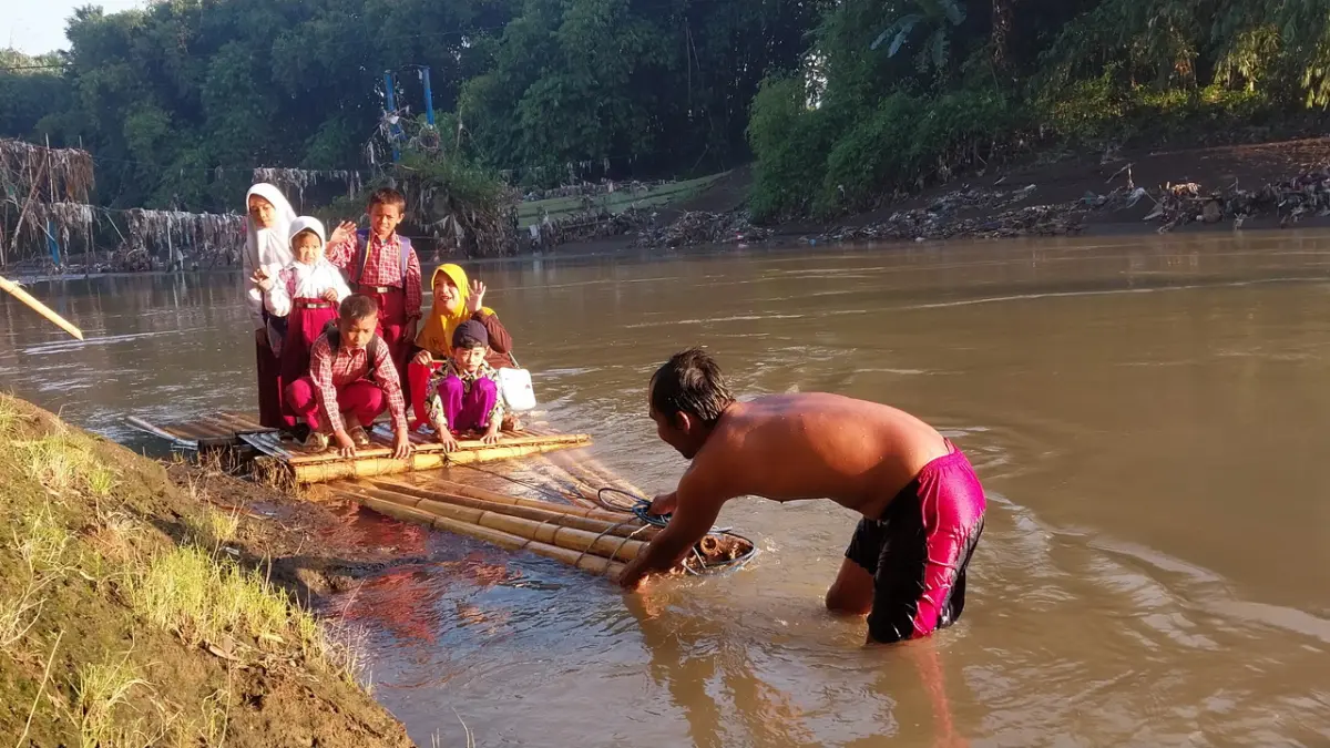 Siswa SD dan TK menyeberangi Sungai Bedadung menggunakan getek bambu untuk berangkat sekolah setelah jembatan penghubung dua dusun di Jember putus. (Radar Jember)