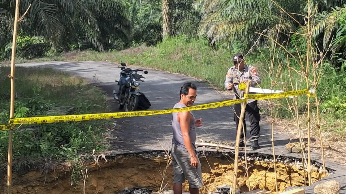 Personel kepolisian memasang tanda peringatan di lokasi jalan amblas di Desa Angan Tembawang, Kecamatan Jelimpo, Kabupaten Landak, Jumat (8/5). Jalan tersebut longsor usai diterjang banjir akibat hujan deras.