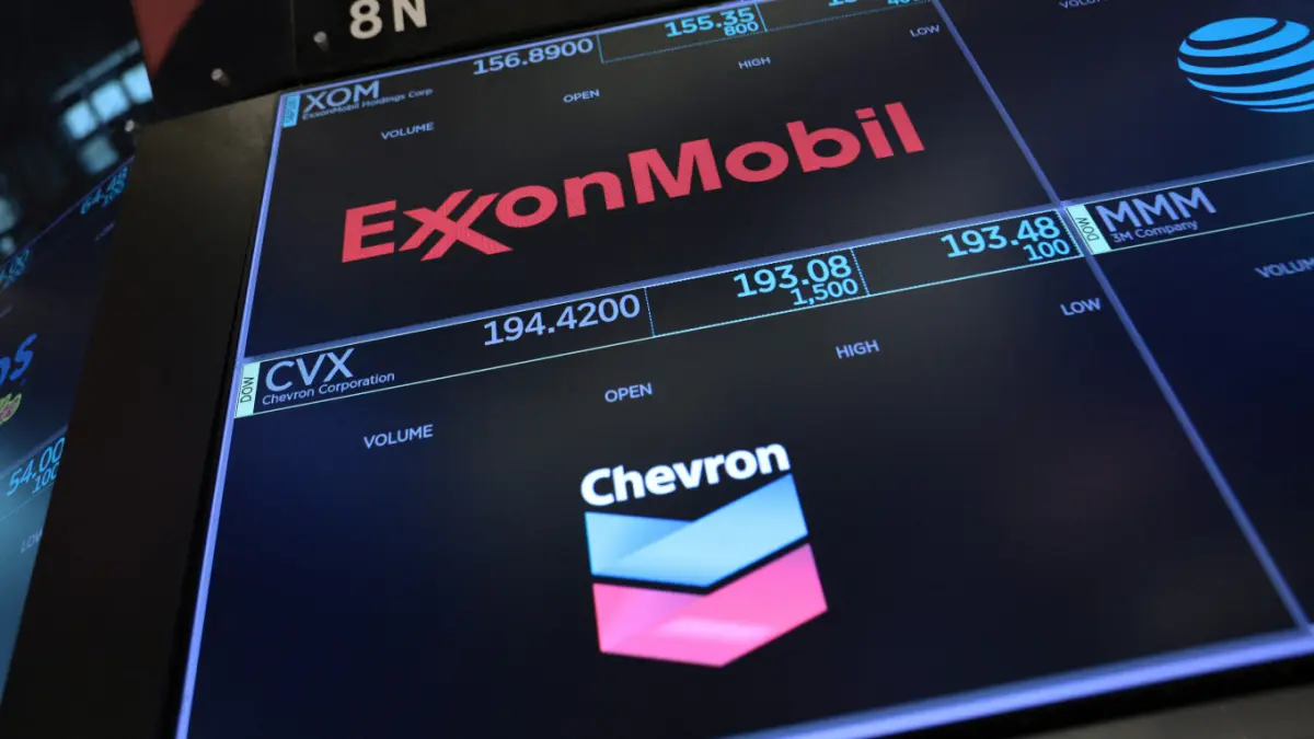 Logo ExxonMobil dan Chevron terlihat di lantai bursa New York Stock Exchange. Kedua perusahaan dituding Presiden Donald Trump menerima keuntungan berlebih akibat kelangkaan pasokan minyak dalam perang antara AS lawan Iran. (MICHAEL M. SANTIAGO/AFP)