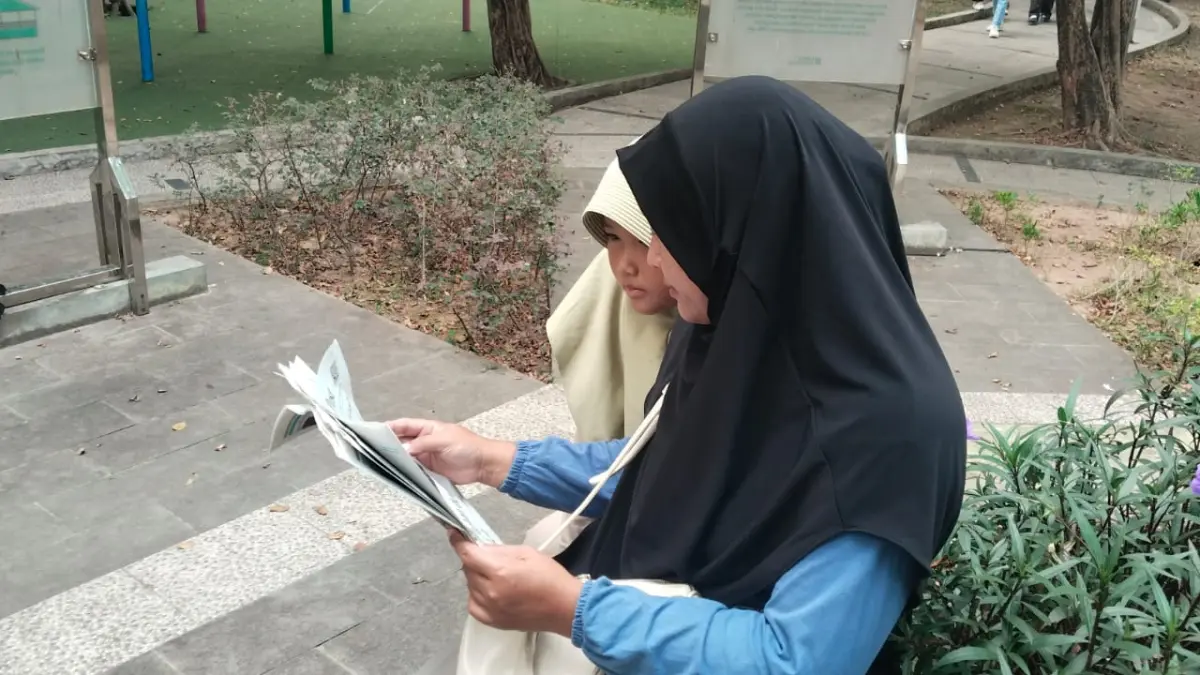 Pikan bersama anaknya membaca koran Pontianak Post di Taman Catur UNTAN, Jumat (21/8). Di tengah pesatnya perkembangan media digital, Pikan menilai Pontianak Post masih menjadi salah satu surat kabar yang banyak dibaca masyarakat. (WANDI/PONTIANAK POST)