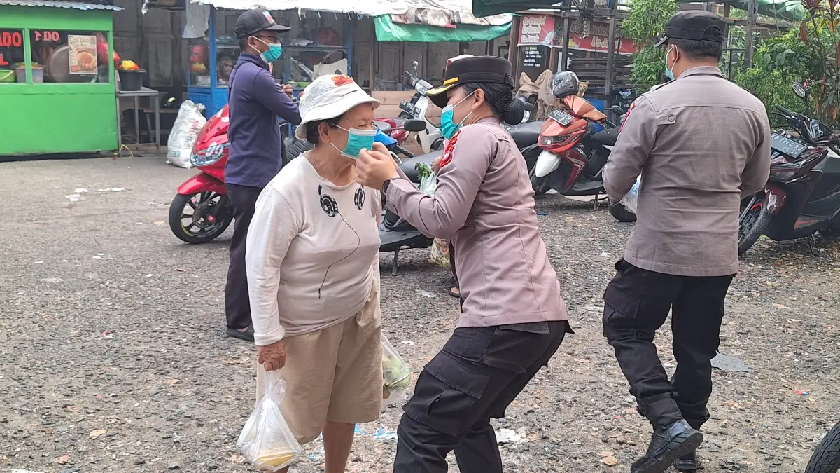 Personel Ditbinmas Polda Kalbar membantu memasangkan masker kepada seorang lansia saat kegiatan penerangan keliling di Kompleks Pasar Kemuning, Pontianak, Rabu (26/8/2026).