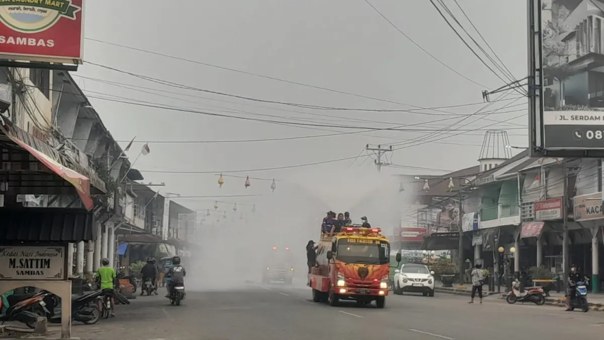 Mobil Damkar semprotkan air ke udara ditengah kabut asap yang masih kuat di Kota Sambas.