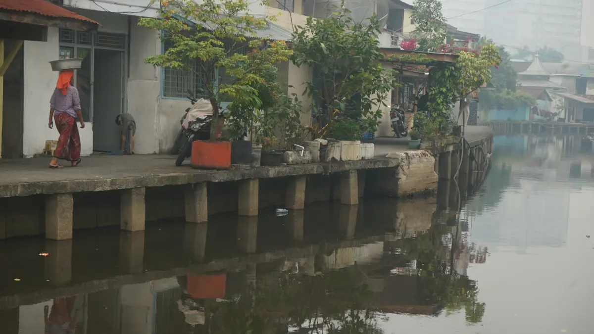 Warga melintas di samping Parit Tokaya yang sedang pasang. Saat kondisi surut air parit mengeluarkan bau yang mengganggu. (HARYADI/PONTIANAK POST)