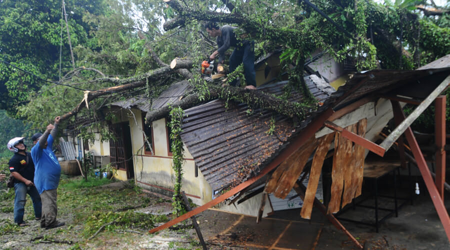 TIMPA RUMAH: Petugas bersama warga  motong batang pohon yang menimpa rumah warga pasca terjadi hujan disertai angin kencang di Jalan Husein Hamzah, Kamis (26/9) |HARYADI/PONTIANAKPOST