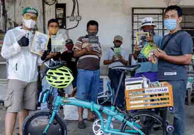 DUA HOBI: Sejumlah warga membaca buku yang dibawa Yunaz di boks bagian belakang sepedanya di depan Pasar Pucang Anom, Selasa (7/7). ALFIAN RIZAL/JAWA POS