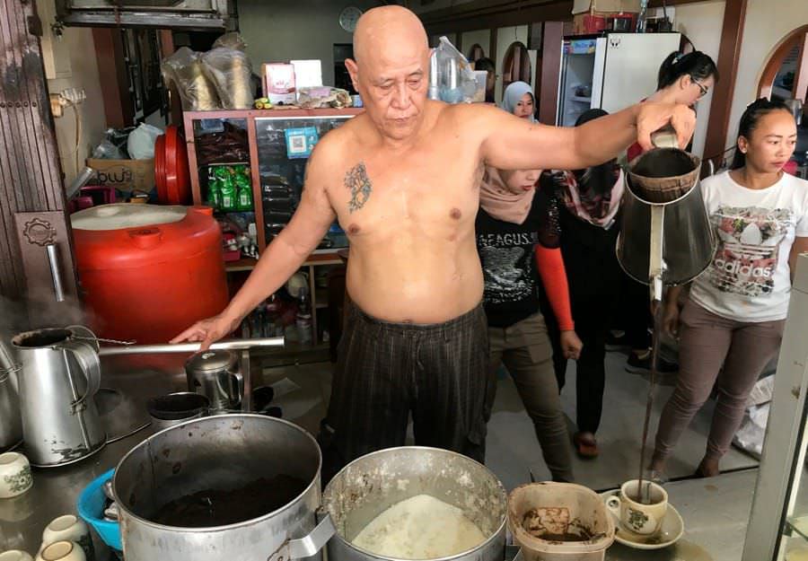 SEDUH KOPI: Asiang saat menyeduh kopi dengan gaya khasnya. Warkop ini  salah satu warkop yang ramai dikunjungi setiap harinya. Sayangnya warkop ini harus ditutp sementara karena pengunjungnya reaktif Covid-19.