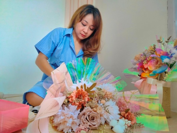 PRODUKSI: Kristin Sisilia sedang menyelesaikan buket bunga yang dipesan oleh pembeli online-nya.    (Aristono/Pontianak Post)