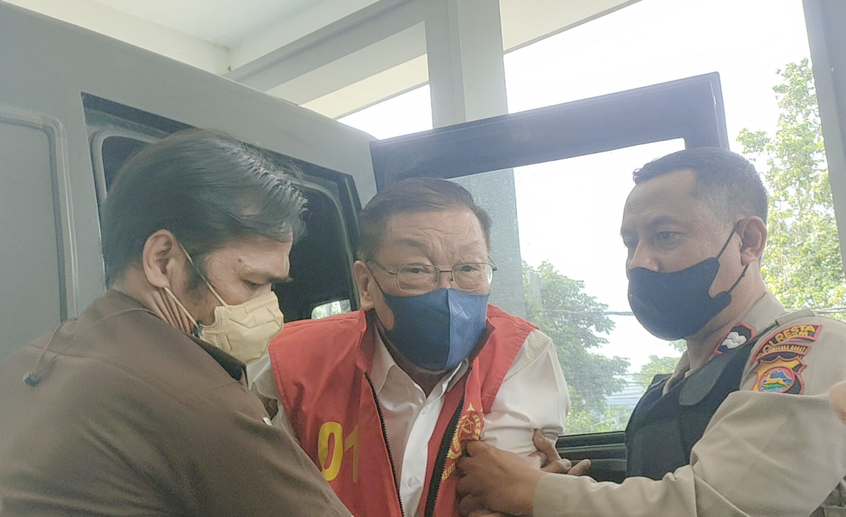 Terdakwa korupsi tambang pasir besi Po Suwandi (tengah) dipapah jaksa dan polisi saat turun dari mobil tahanan kejaksaan.