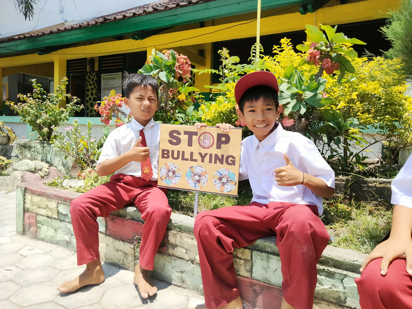 Dua murid SDN 2 Paokmotong berfoto di dekat banner Stop Bullying yang ditancapkan di halaman sekolah.