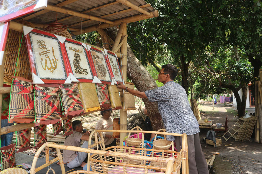 Bahrudin memeriksa kondisi barang kerajinan yang dijual di depan rumahnya.
