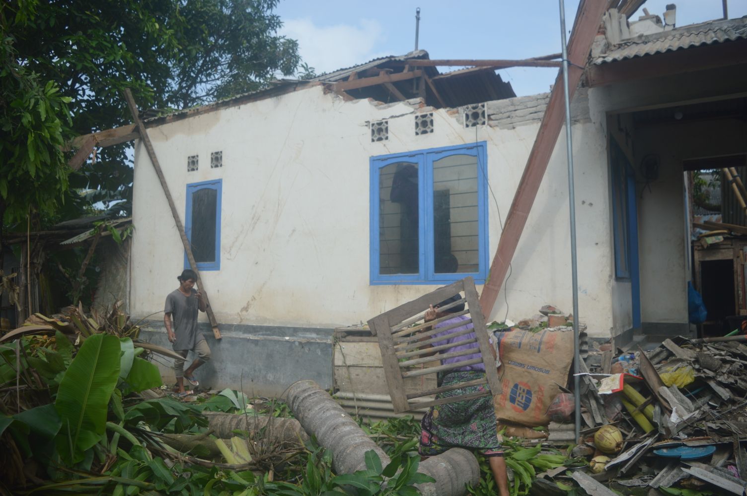 Ramdani (kiri) dibantu warga membersihkan puing rumah yang porak poranda akibat pohon tumbang saat hujan disertai angin kencang di Dusun Bererong, Desa Nyerot, Kecamatan Jonggat, Loteng.