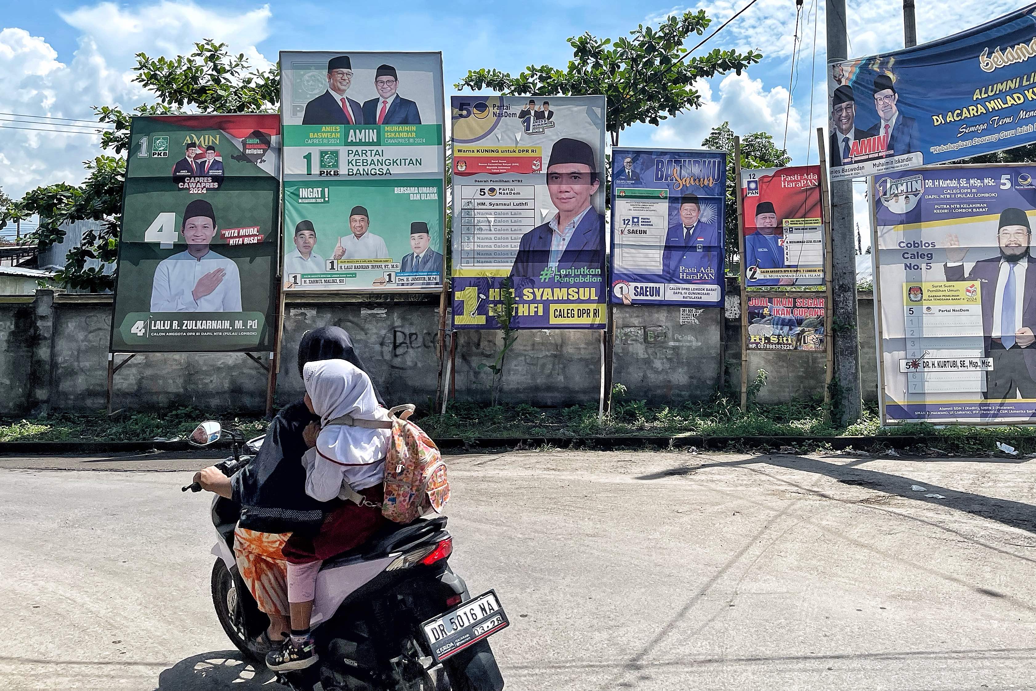 APK: Seorang pengendara sepeda motor membonceng anaknya melewati jalan yang dipenuhi Alat Peraga Kampanye (APK) di wilayah Kota Mataram, belum lama ini.