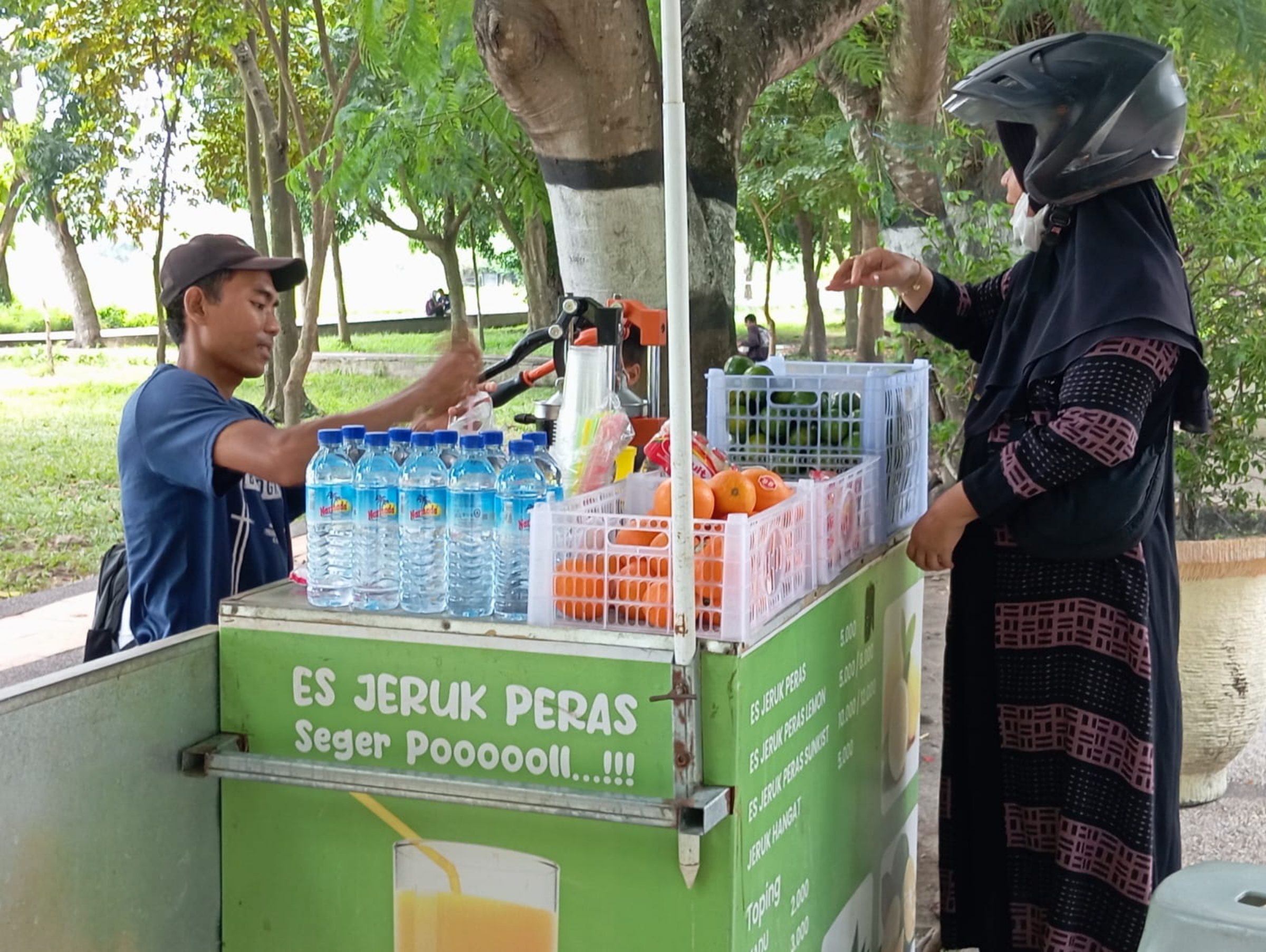 LAYANI PEMBELI: Penjual minuman tiga varian jeruk peras, Sukriadi tengah melayani pembeli di Udayana. (FERIAL/LOMBOK POST)