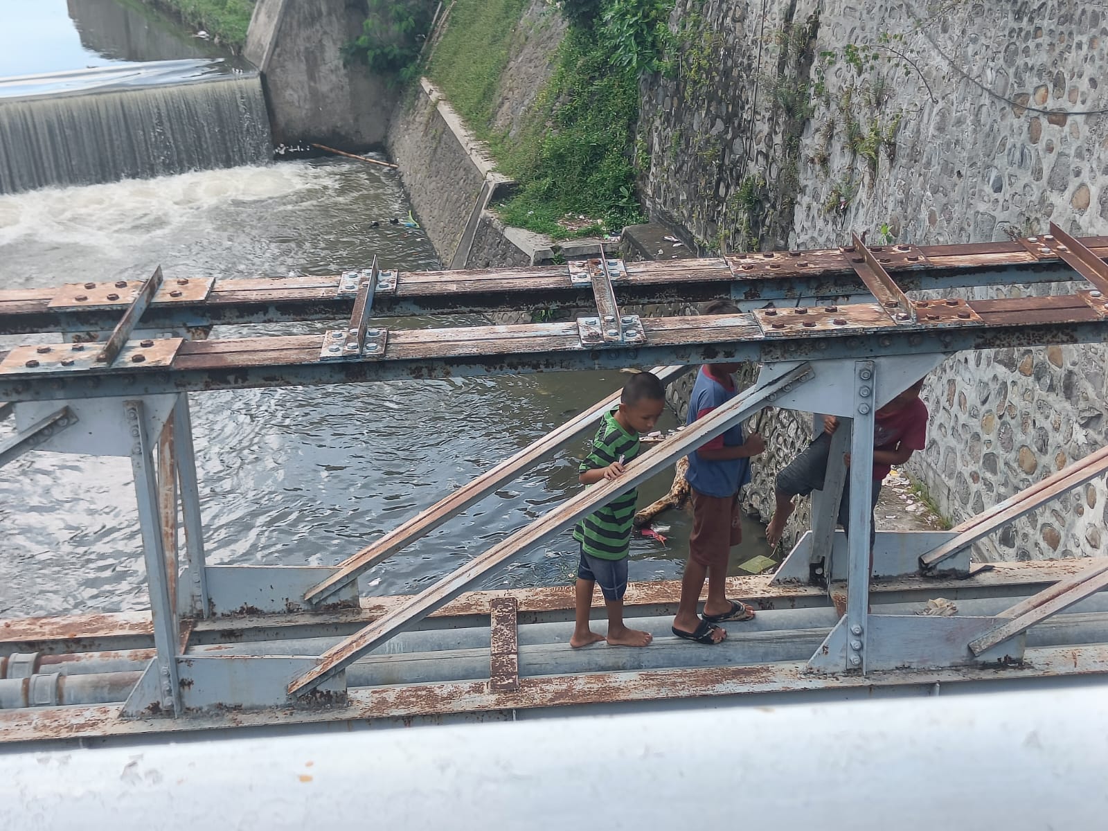 BAHAYA: Tiga orang anak tengah menyusuri rangka saluran pipa air bersih yang berada di atas salah satu sungai besar di Kota Mataram, samping toko Boxi.