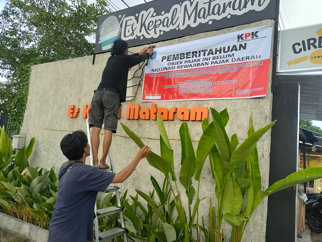 SANKSI SOSIAL: Petugas BKD Kota Mataram memasang banner tanda penunggak pajak dari KPK di Es Kepal di Mataram, beberapa waktu lalu.(HARLI/LOMBOK POST)