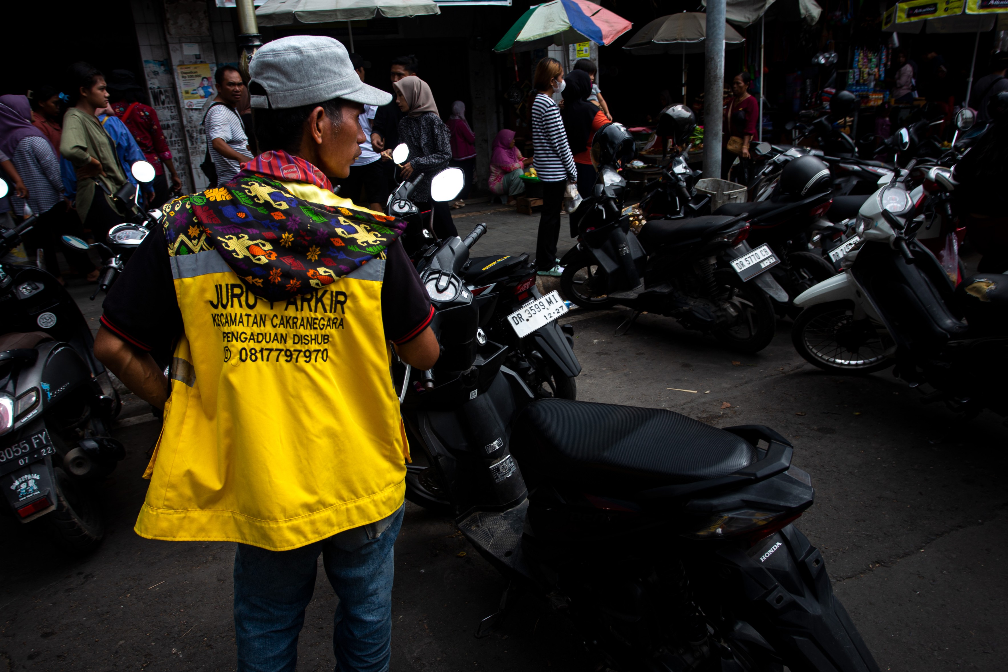 HARUS TETAP BAYAR RETRIBUSI YA: Seorang juru parkir memantau situasi kendaraan di lokasi parkir Pasar Cakranegara, beberapa waktu lalu.(HARLI/LOMBOK POST)