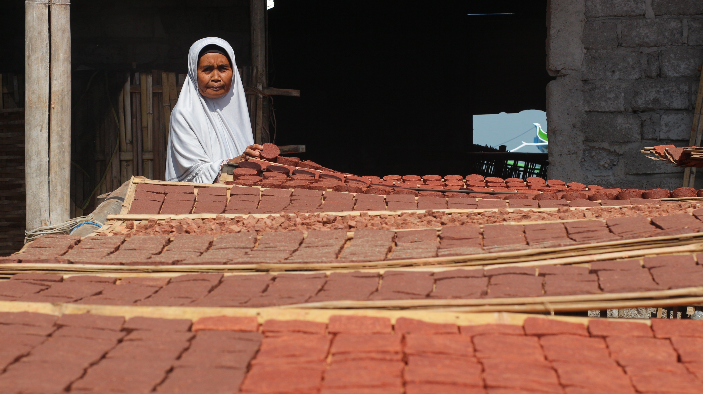 CEK: Hj Aminah melihat terasi udang yang dijemur di pekarangan rumahnya. (SUPARDI/LOMBOK POST)