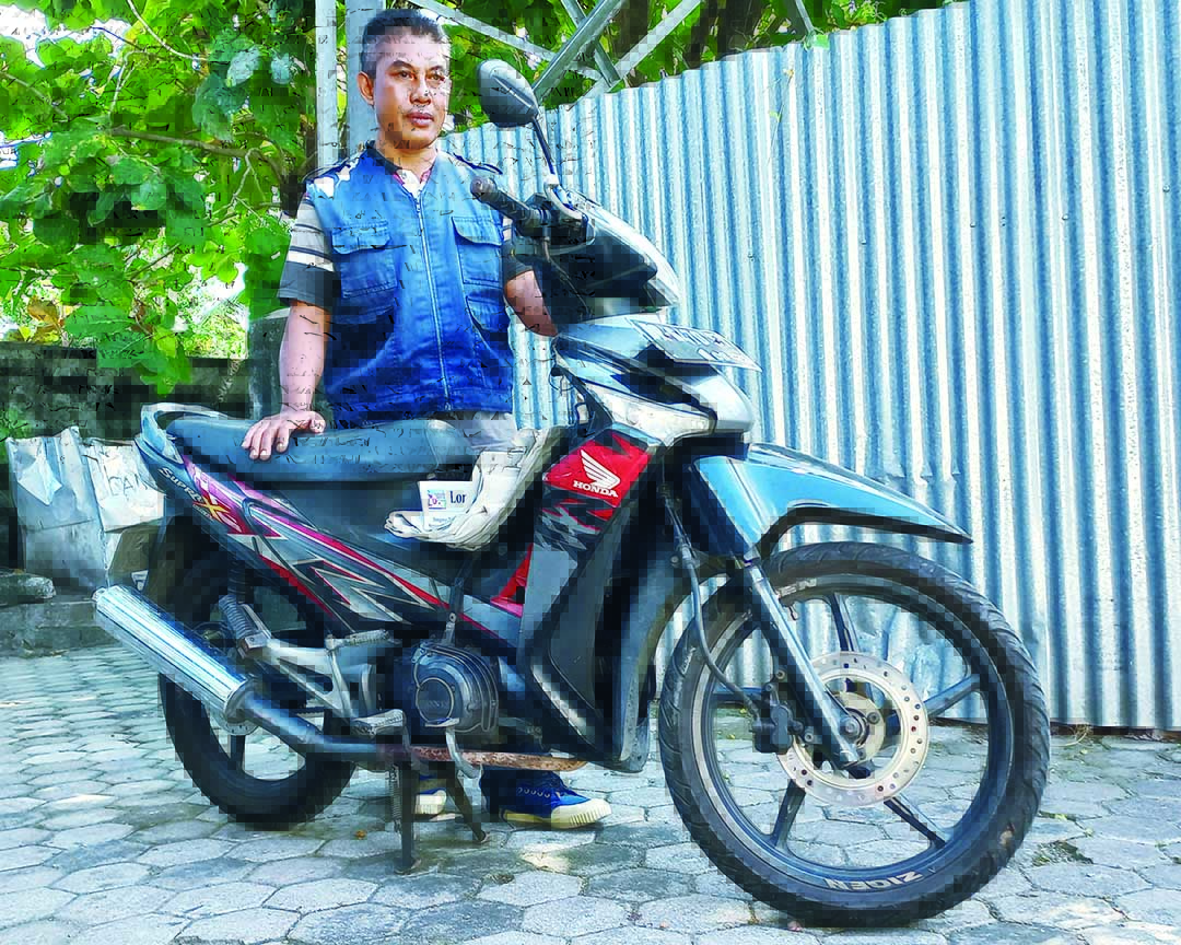 SETIA MENEMANI: Iswandi dengan Honda Supra X-nya di sela-sela istirahat setelah mengantar koran.(Galih/LombokPost)