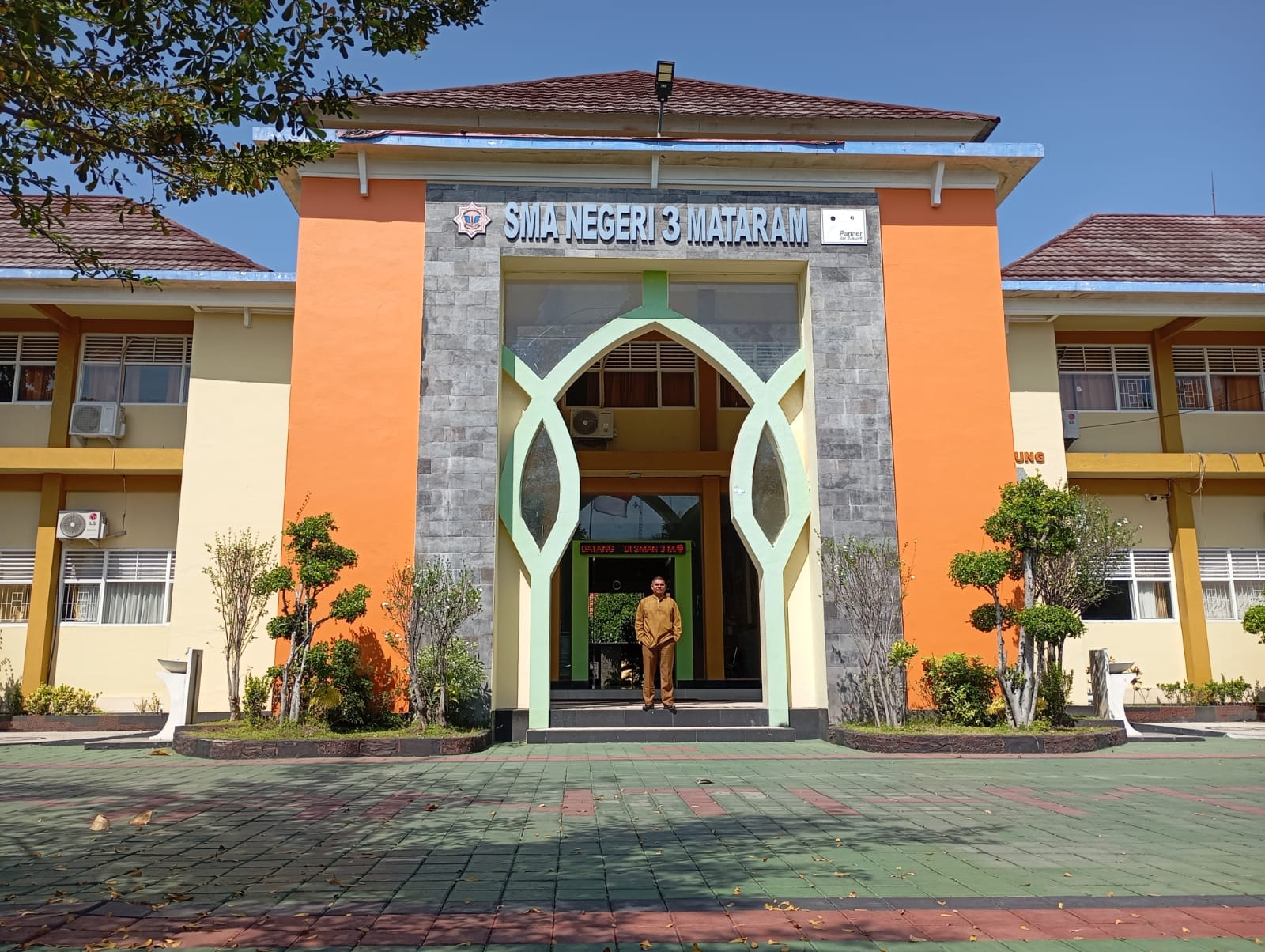 SEKOLAH PASCH: Seorang pegawai SMAN 3 Mataram berdiri di depan pintu masuk sekolah setempat, kemarin (26/7). (ROJAI/LOMBOK POST)