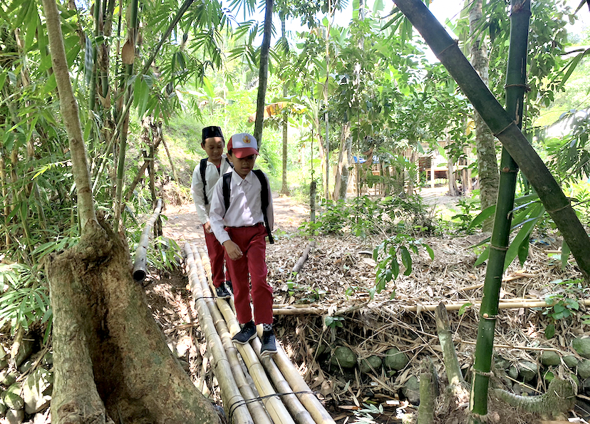 TERPENCIL: Dua murid sekolah yang sedang melintasi jembatan kecil bambu untuk pulang ke rumahnya di Dusun Landungan, Desa Guntur Macan, kemarin (19/8).  (CHIA/LOMBOK POST)