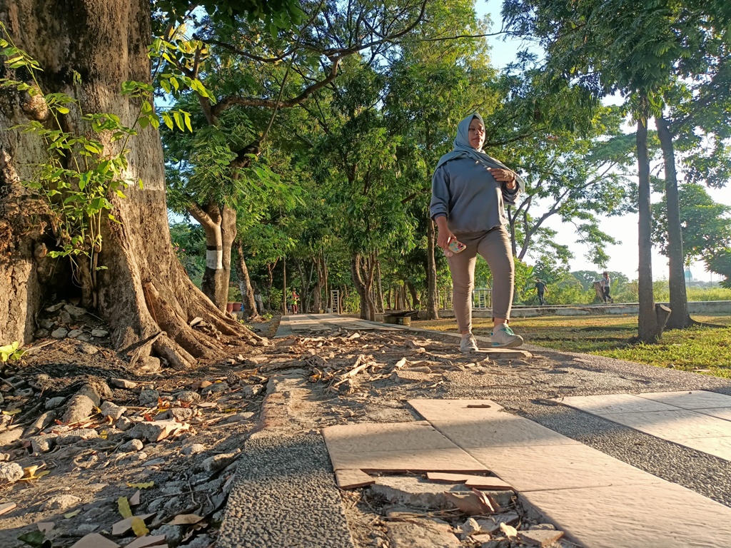 HARUS DIPERBAIKI: Seorang pengunjung harus berjalan hati-hati ketika melintas di lintasan jogging Udayana yang dalam kondisi bopeng, Minggu (27/10).