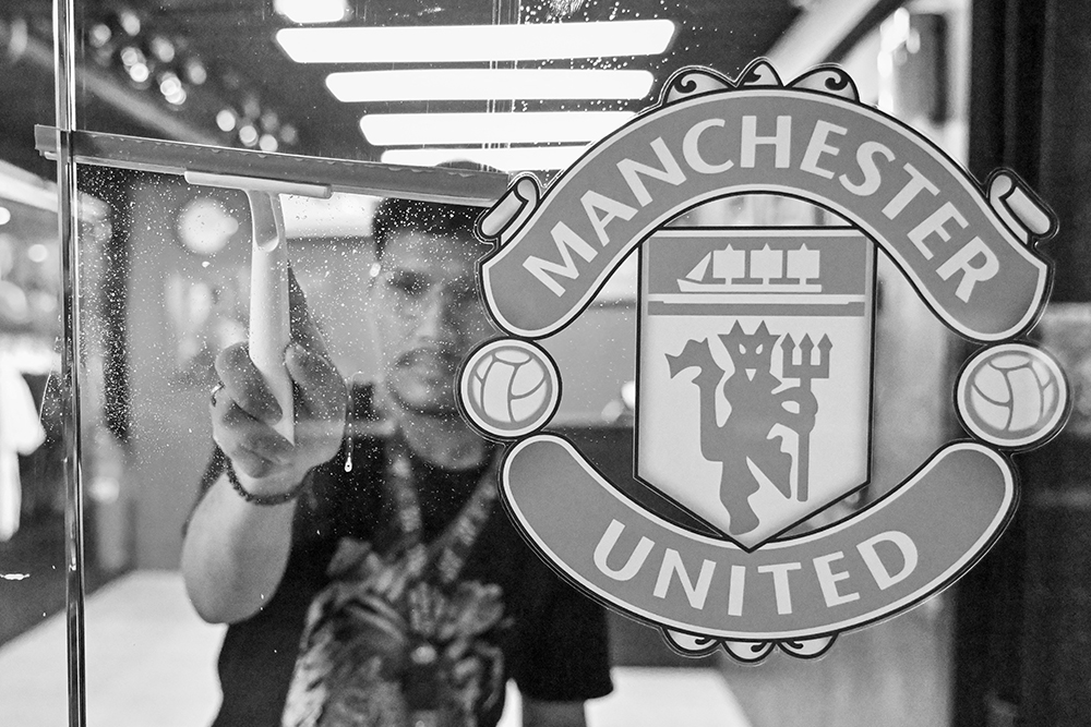 Zulfikar Rahman, Store Officer & Graphic Designer of the Indonesian Manchester United football club fan shop and base camp for the United Army community, cleans as the store opens for business in Jakarta on October 29, 2024. (Photo by BAY ISMOYO / AFP